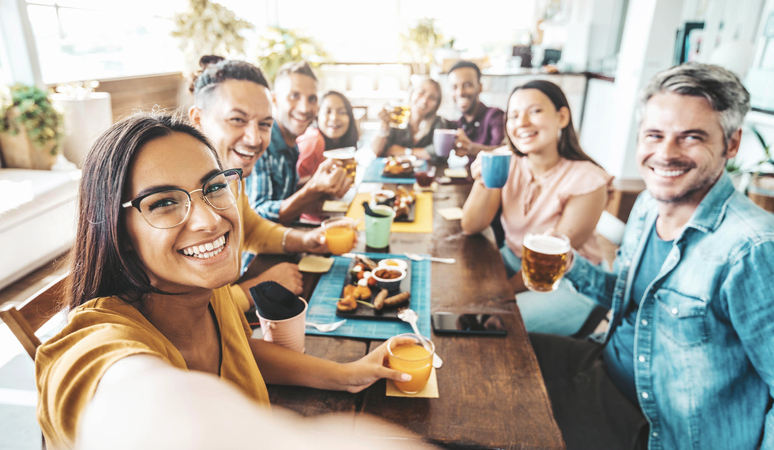 Multiracial group of friends having dinner party sitting at coffee bar table - Young people enjoying meal on morning brunch time - Life style concept with women and men at lunch break cafe bar